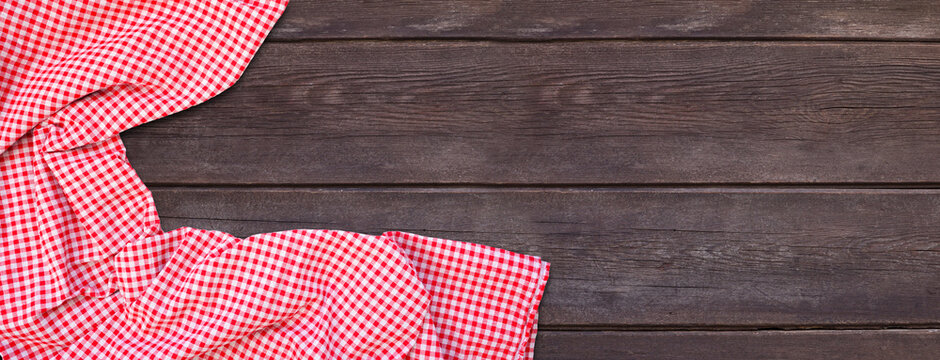 Picnic theme dark wood background with red and white check cloth corner border. Top down view banner. Copy space.