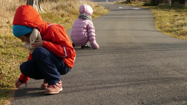 Two little beautiful girls walk in winter clothes collect gravel on the path.