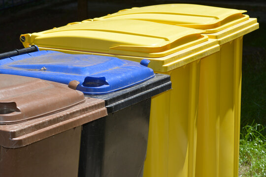 A row of plastic waste sorting bins in yellow blue brown and black colors for recycling management outdoors