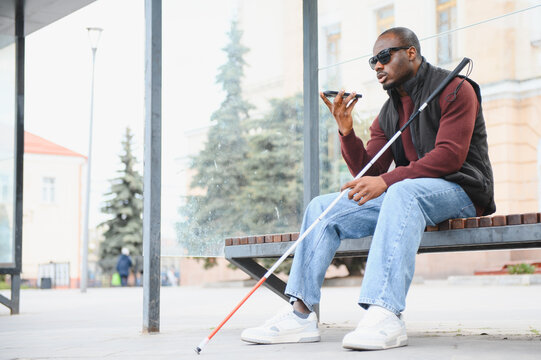 Blind african american man using smartphone at bus stop