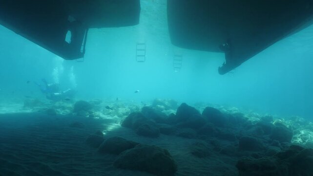 scuba diver scenery under the parked boats with sun beams and rays underwater