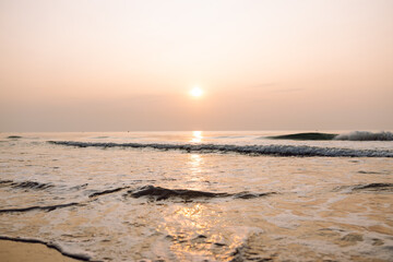 Obraz premium Sunset on the beach, gentle waves, and buildings in the distance along the coastline. Seascape. A tranquil landscape, sea waves at sunset. Concept of nature and beauty.