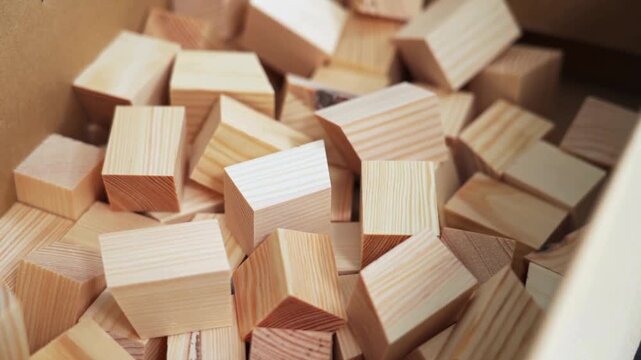 Natural wooden blocks in cardboard box, unfinished timber toy pieces for DIY crafts, pile of light pine wood cubes for building and education