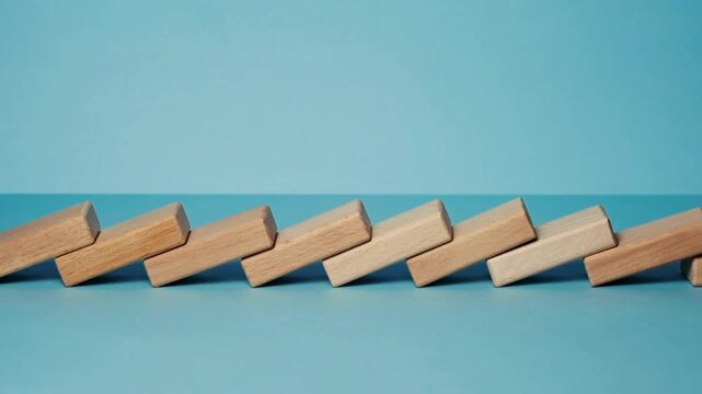 Domino effect of wooden blocks falling in sequence, chain reaction of timber bricks on blue background, business risk and crisis management concept