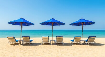 Fototapeta premium Serene tropical beach scene featuring blue parasols and white reclining sunbeds arranged on golden sand under a clear sunny sky by the sea, tropical, lifestyle, horizon