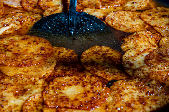 Traditional indian malpua sweets frying in a large pan with syrup. Closeup of golden brown malpua pancakes being deep fried and soaked in sugar syrup with a slotted spoon on a street food market