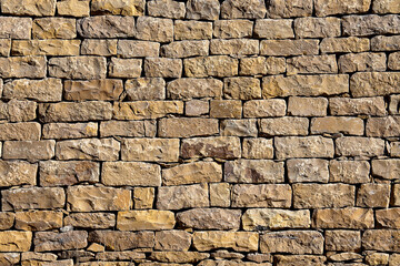 Fototapeta premium Rustic ancient dry stone wall texture background. Full frame background texture of traditional dry stone wall built from rough natural brown sandstones without mortar