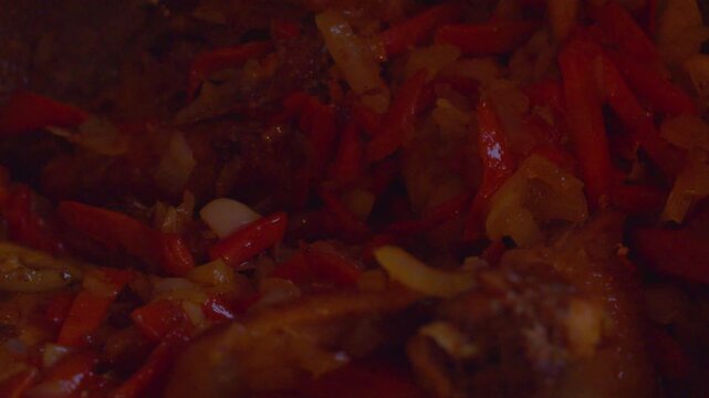 A close-up shot from above: chicken pieces and vibrant vegetables sizzle in a hot cast-iron pot. The process of cooking at home.