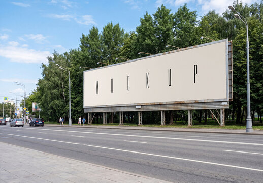Large horizontal outdoor billboard mockup standing along a city highway road with green trees and blue sky background