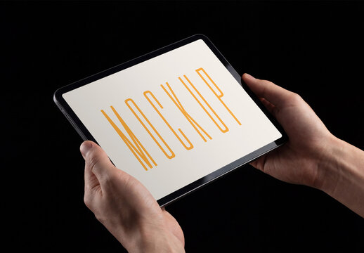 Hands holding a modern digital tablet computer mockup with blank screen isolated on a black background