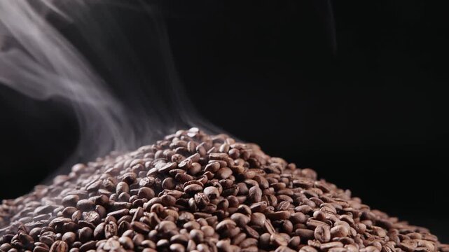 Slow motion steaming coffee beans pile on dark studio background with low angle pan closeup.