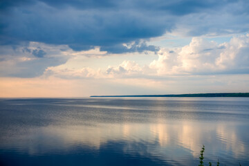 Obraz premium Dramatic storm clouds above calm reservoir water with sunset reflections and peaceful evening landscape