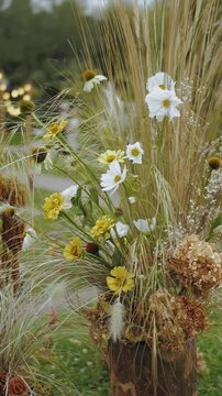Vertical video. Wildflower arrangement with daisies and dry grass during outdoor wedding setup. Floral decor in natural evening light. Filmed in 4K slow motion.