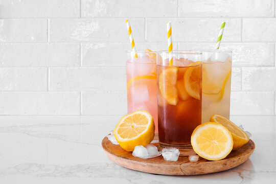 Refreshing summer drinks, pink lemonade, iced tea and lemonade in a tray with lemons. Side view on a bright background.