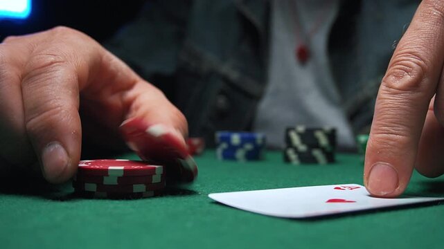 Male poker player places red chips on green felt table while revealing a playing card, showcasing a strategic moment in a card game setting