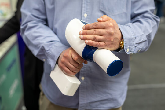 Man holding portable dental X-ray device. Close-up of a man demonstrating a white and blue handheld dental X-ray device in a clinical trade show setting.