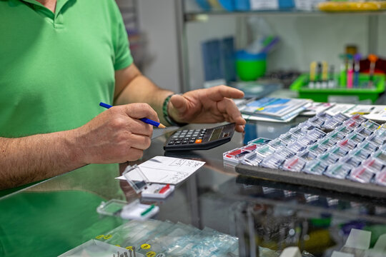 Dental technician calculating inventory costs. Close-up of a person using a calculator and pencil while organizing dental supplies and color coded inventory trays.