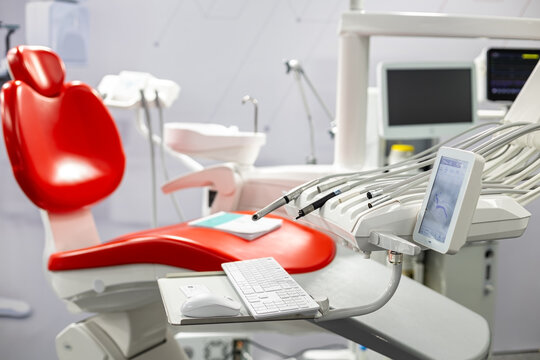 Modern Dental Chair with Treatment Equipment. Bright dental clinic interior with a red patient chair, treatment tools, digital screen, and modern medical equipment.