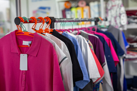 Colorful Polo Shirts Hanging in Store. Close-up of colorful polo shirts on hangers in a retail clothing shop with blank price tag and soft background.