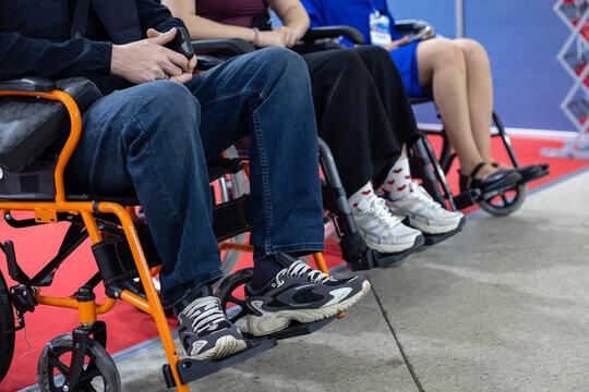 People Sitting in Wheelchairs at Event. Close-up of people seated in wheelchairs at an indoor exhibition or medical equipment event, showing mobility and accessibility.