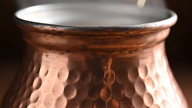 Closeup of a hammered copper Turkish coffee pot with steam rising.