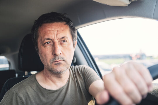 Middle-aged man driving a car with a focused, thoughtful expression as he grips the steering wheel during a daytime commute or road trip.