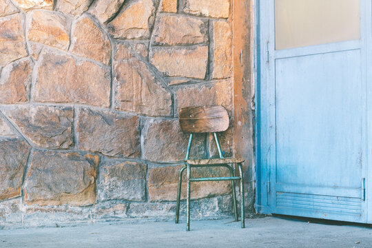 Vintage wooden chair against stone wall beside weathered blue door in rustic outdoor scene