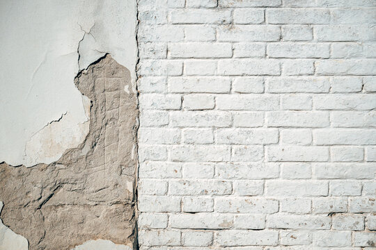Weathered exterior wall divided between exposed worn plaster and white brick masonry, showing cracks, erosion and aged urban texture.