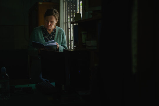 Woman standing in dim interior of an old office reading a book, quiet introspective moment in soft ambient light