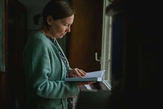 Female librarian reading near window in vintage office setting, natural light highlighting calm scholarly environment