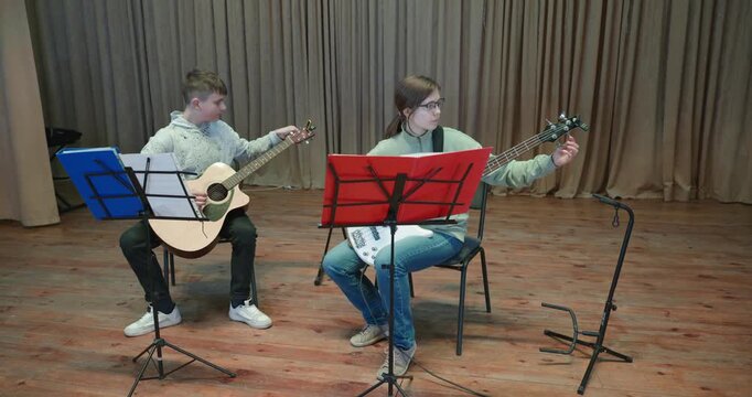 Boy and Girl Practice Playing Music on Stage. Kids Play Guitar and Bass Guitar. 4K 10-bit