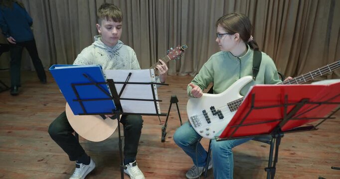 Boy and Girl Practice Playing Music on Stage. Kids Play Guitar and Bass Guitar. 4K 10-bit
