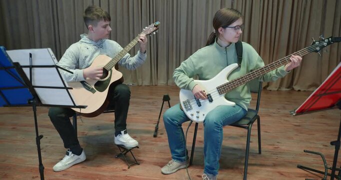 Boy and Girl Practice Playing Music on Stage. Kids Play Guitar and Bass Guitar. 4K 10-bit