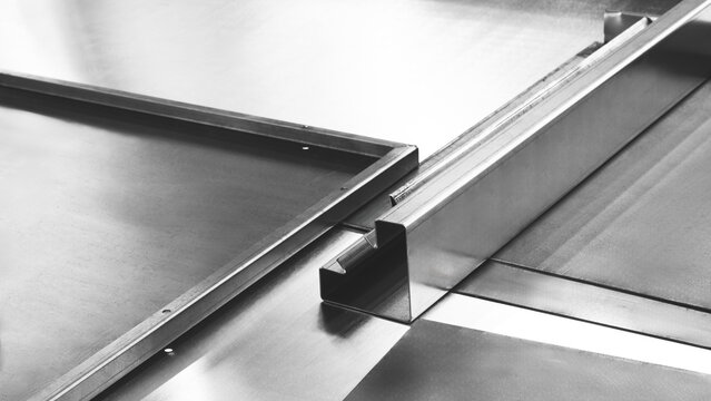 Shiny metal sheets lie on the table of an industrial laser cutting and bending machine. Industrial background