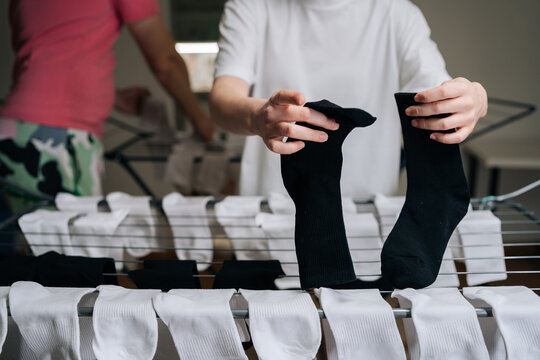 Close-up young couple hanging freshly washed laundry on clothes drying rack, placing clean white and black socks on metal bars, performing household chores and daily routine tasks, close-up.