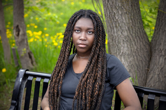 Young African woman sitting on bench in green park, summer portrait