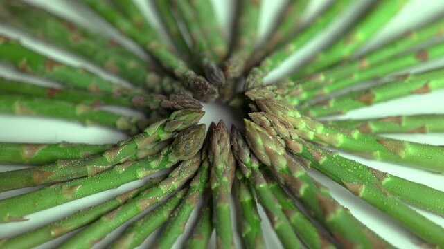 Fresh green asparagus shoots arranged in a circular pattern turning and spinning slowly on white background