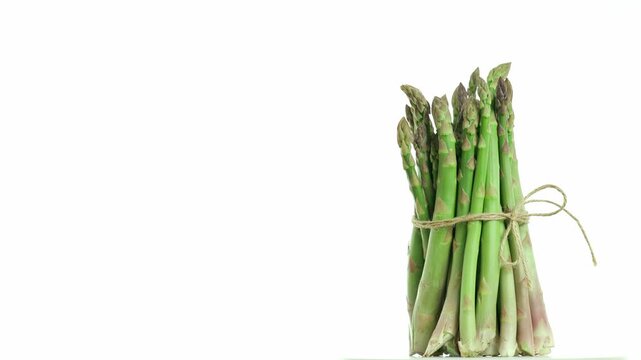 Bunch of  asparagus officinalis tied with string turning and spinning presenting edible shoots on white background