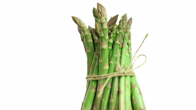 Fresh nutritious bunch of green asparagus bound with twine turning and spinning slowly revealing edible shoots on a white background