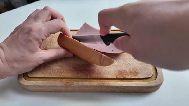 Close up shot of hands using a sharp kitchen knife to cut slits into a fresh sausage on a wooden chopping board. Food preparation process.