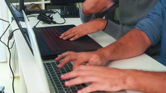 Two focused software engineers collaborating on code in modern office, professional developers discussing project on laptop and computer screen