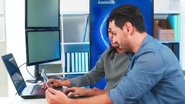 Two focused software engineers collaborating on code in modern office, professional developers discussing project on laptop and computer screen