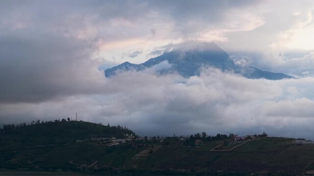 Dramatic imbabura volcano partially covered by moving clouds over the hills of yahuarcocha lake
