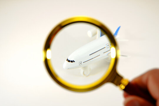 This photograph captures a close-up view of model airplane, its intricate details brought into sharp focus by a magnifying glass held by person's hand, suggesting a detailed inspection or examinations