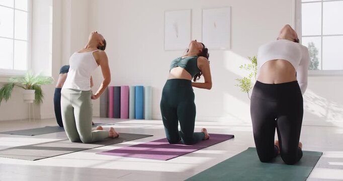 Yoga group in studio class practicing pose. Women kneel on mats in camel backbends, guided training. Focus on alignment, breathing, and flexibility. Clear concept: mindful group fitness.