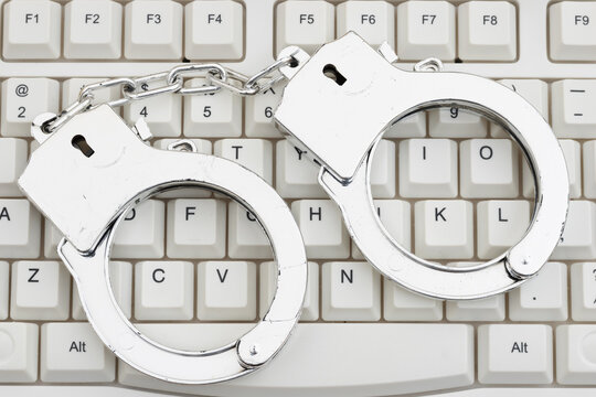 Handcuffs on a white computer keyboard for law enforcement of digital scams