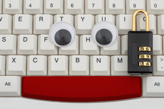 Googly eyes with combination lock on a white computer keyboard for data surveillance