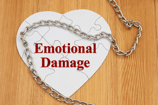 Emotional damage text on a white puzzle heart with metal chain on a wood desk for divorce