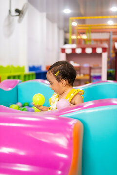 A small baby playing in a colorful ball pit at an indoor playground, reflecting fun, curiosity and sensory exploration, baby 1 to 2 years old.