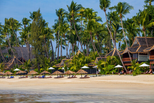 Luxury beach resort with traditional bungalows on Ngapali beach, Myanmar. Beautiful sandy coastline of Ngapali beach featuring wooden resort bungalows, sun loungers, straw umbrellas and palm trees